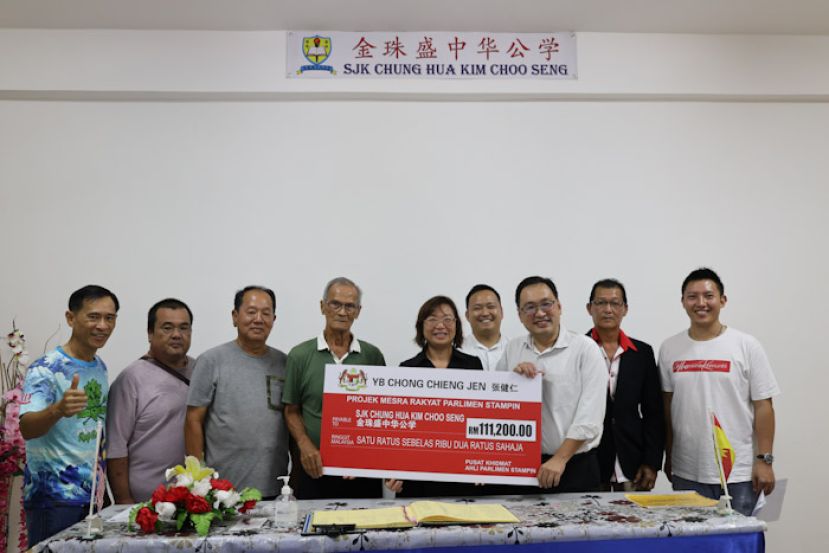 实旦宾区国会议员张健仁(右3)在众校董、老师们和助理的陪同下，移交11万1200令吉的拨款支票给石角金珠盛中公校董会主席赖双利。右起为张健仁特别助理沈杰龙、行动党石角支部主席陈恪浩、张健仁特别助理江峰年及江素华校长。