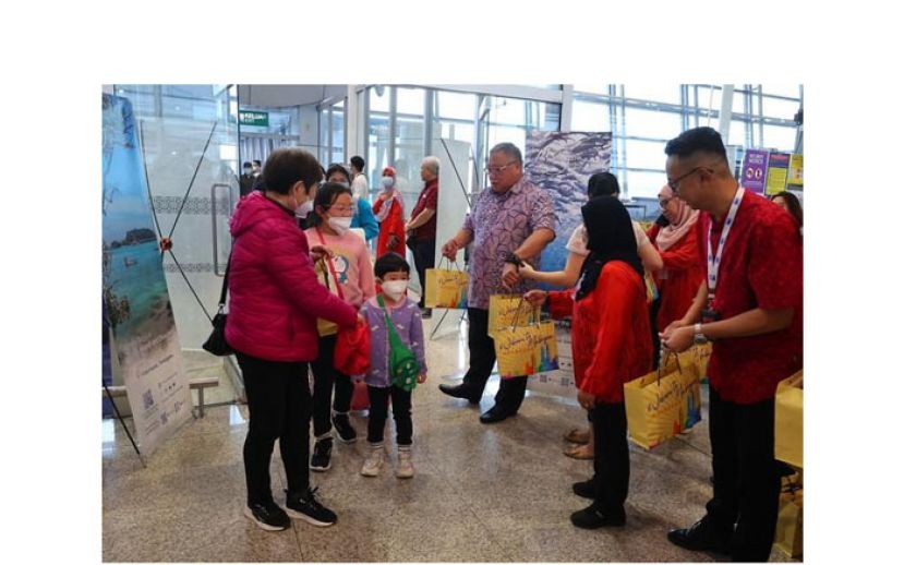 张庆信在机场派发新年纪念品给到访的中国游客。