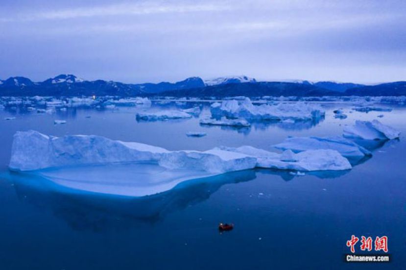 2019年8月15日夜间，一艘船在格陵兰岛东部库鲁苏克镇附近的大型冰山旁航行。