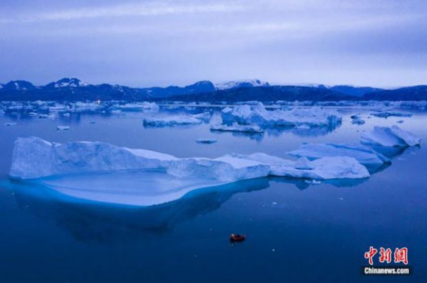 2019年8月15日夜间，一艘船在格陵兰岛东部库鲁苏克镇附近的大型冰山旁航行。