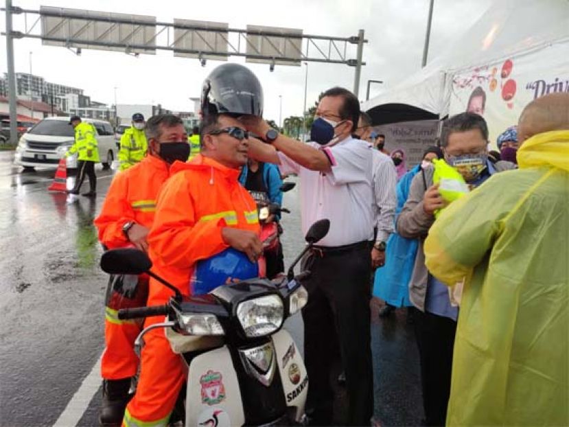 砂交通部部长拿督斯里李景胜为电单车骑士戴上头盔时摄。