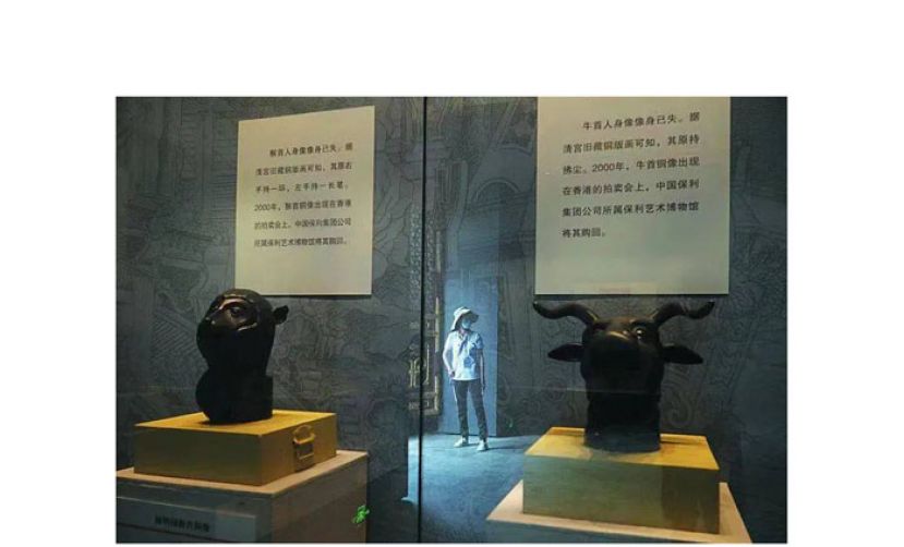 正觉寺兽首仿制品展示柜玻璃上反射出一位女士的身影。