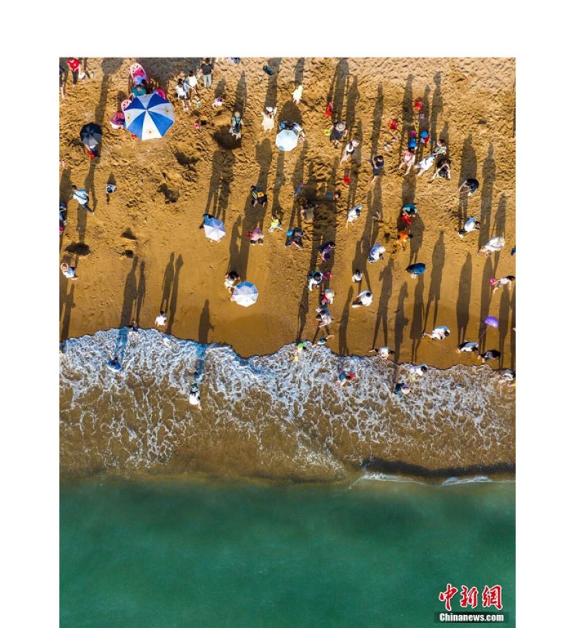 鱼鳞洲上，暖金色细沙柔软如绒。游人或赤脚逐浪，或闲坐休憩，悠长的影子勾勒出慵懒的轮廓。