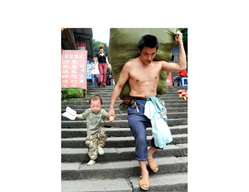 2010年6月20日，摄影师许康平在重庆朝天门码头拍下冉光辉牵着儿子扛货的照片。