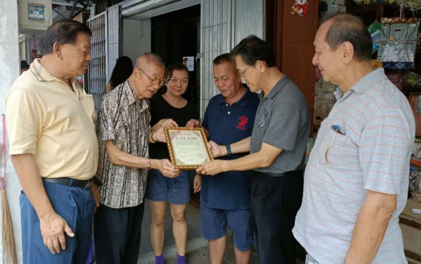 薛华东（右2）等人在看甲必丹林传政（右3）和沈云豹（左2）当年在亚答街一店屋发生火患时救人所获表扬状；左为陈中兴、左3是沈青娇及孙守生（右1）。