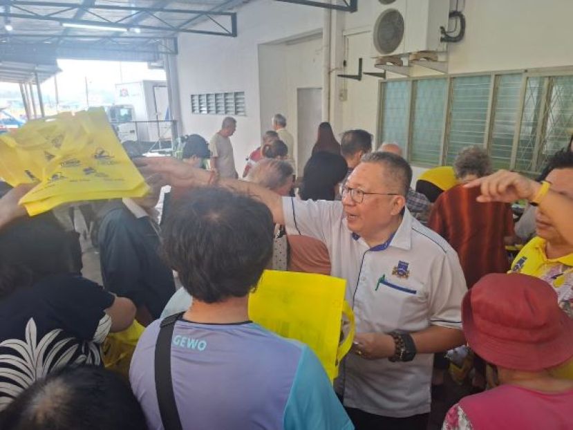 古晋南市市长拿督黄鸿圣（右）在肯雅兰民众联谊会举办的昌明慈悯促销活动上派发环保袋，方便民众购物。