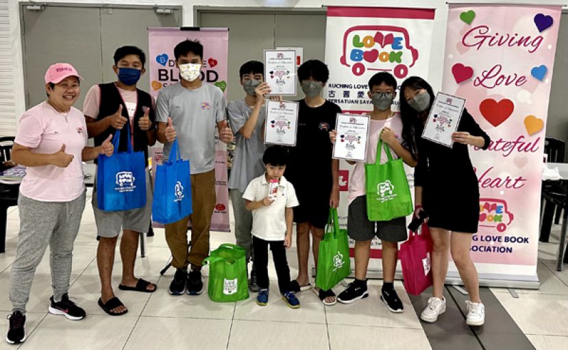 古晋爱心书协会创办人兼主席吕晗韵（左一）及理事们于该会去年十二月三日的捐血活动中赞扬这些学生志愿者的爱心参与。