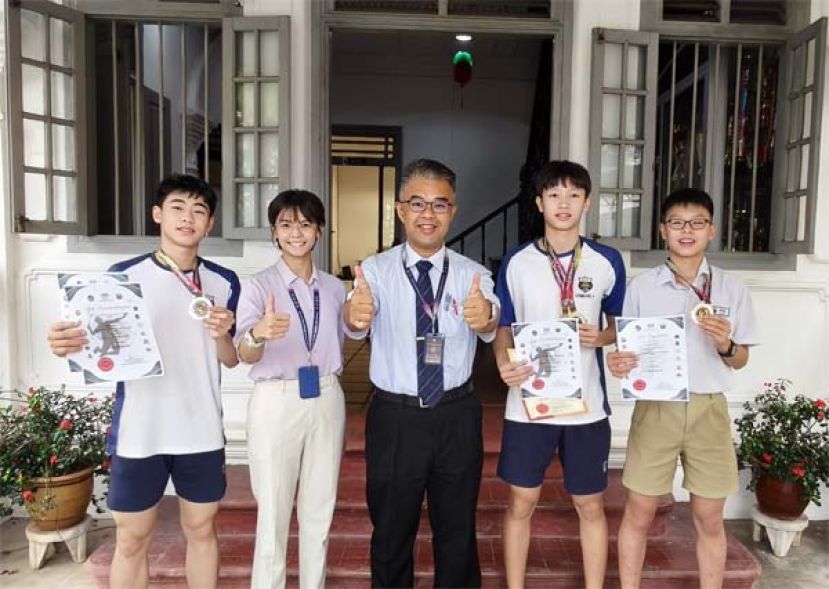 古晋四中的三位杰出羽球健儿张晏诚（右2）、吴宗泽（左1）及张祐嘉（右1）与官晨阳校长（中）及联课主任莫静瑶老师（左2）分享他们在本届代表古晋省出征《2026年全砂学联羽球赛》获奖喜悦。