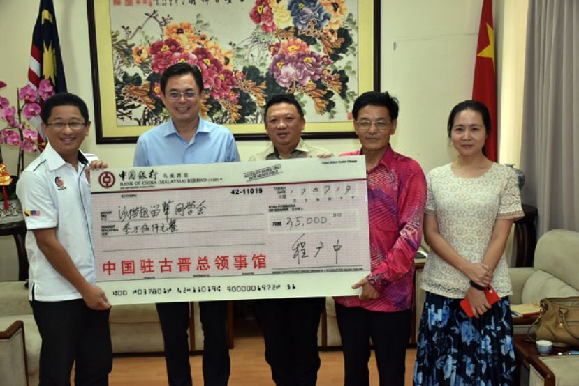在砂地方政府与房屋部长拿督沈桂贤代表陈开（左二）见证下，中国驻古晋总领事程广中（右二）将模拟支票移交予砂拉越留华同学会总会会长黄首咏（左一）。