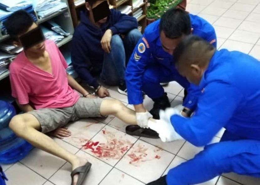 一名嫌犯左腿受伤，由赶到警局的民防局人员包扎伤口。