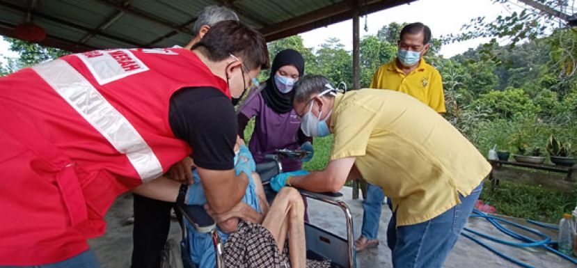 拿督斯里沈桂贤为一位行动不便老人注射疫苗，右是人联党石角支部代主席林亚德。