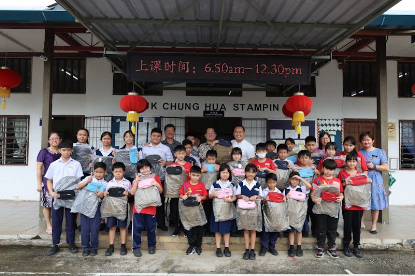 实旦宾区国会议员张健仁特别助理江峰年（中）移交新书包和文具给实胆彬中华公学校长方都儿，并与学子们及老师合影。