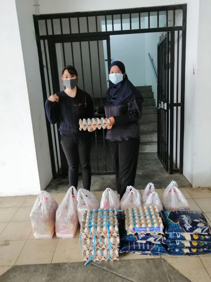 黄培慧（左）分配米粮食品给7间在古晋民丹俄路建筑工程的木屋居民贫户家庭，并由木屋居民代表耳拉（右）代收。
