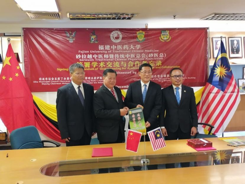 邢伟平总领事（右2）由砂医总会长江宗兴手中接过纪念锦旗；右为诗巫市议会署理主席伊斯干达；左是福建中医药大学副校长苏友新。