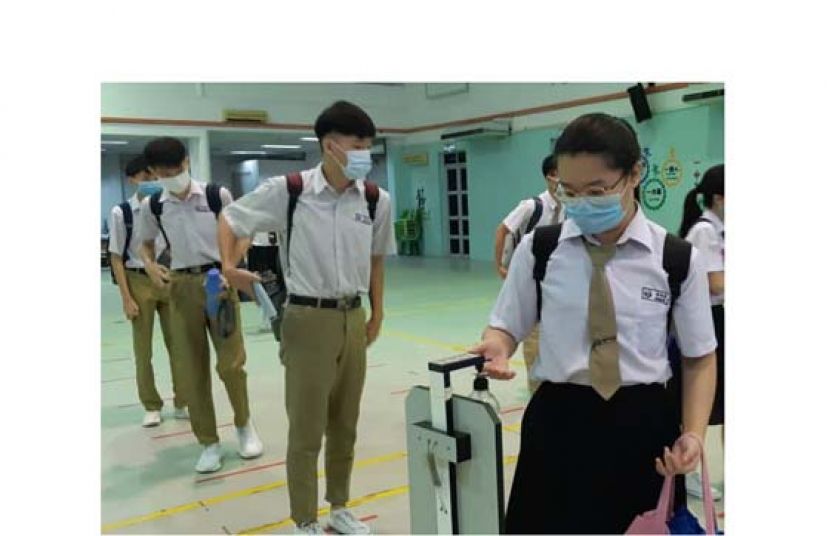 学生佩戴口罩，保持安全距离，排队使用消毒液洗手。