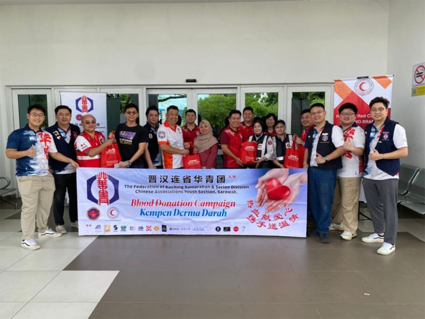 到场的主办单位人员及华青团代表大合照，并由古晋潮州公会青年团顾问周文盛（左六）、青年团团长郑元漳（右四）、筹委主席陈冠中（右七），以及古晋区红新月会的代表（左三）一起移交礼品给成功捐血者。