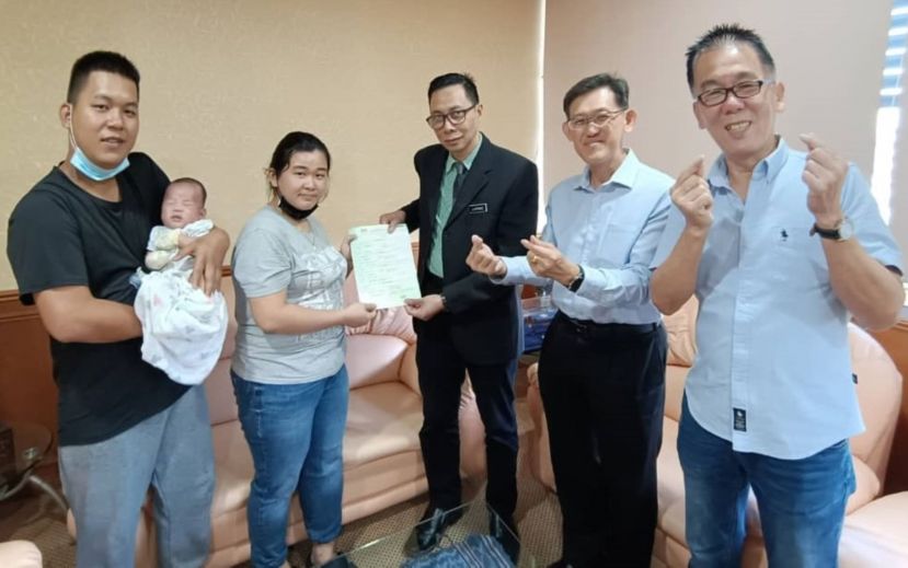 刘美彩（左2）从国民登记局砂局长阿旺阿菲欧（中）手中接过爱儿报生纸；左为丈夫张成福与小志杰；右起为夫妇俩友人杨义顺，砂人联党中央副主席薛华东。