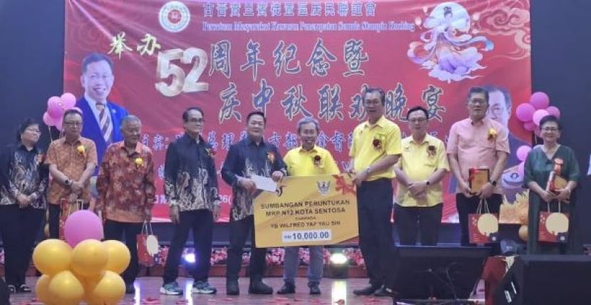 在众嘉宾的见证下，哥打圣淘沙区议员叶耀星（右四）将模拟支票移交予古晋实旦宾徙置区居民联谊会大会主席甲必丹温文明（右六）时摄。