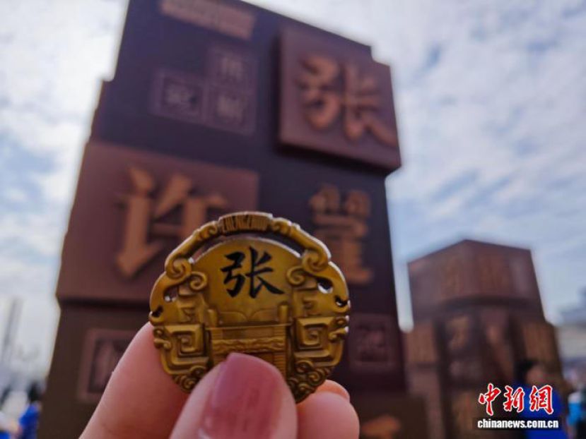 2025郑州马拉松开跑前，参赛选手在姓氏墙前展示姓氏元素纪念牌。