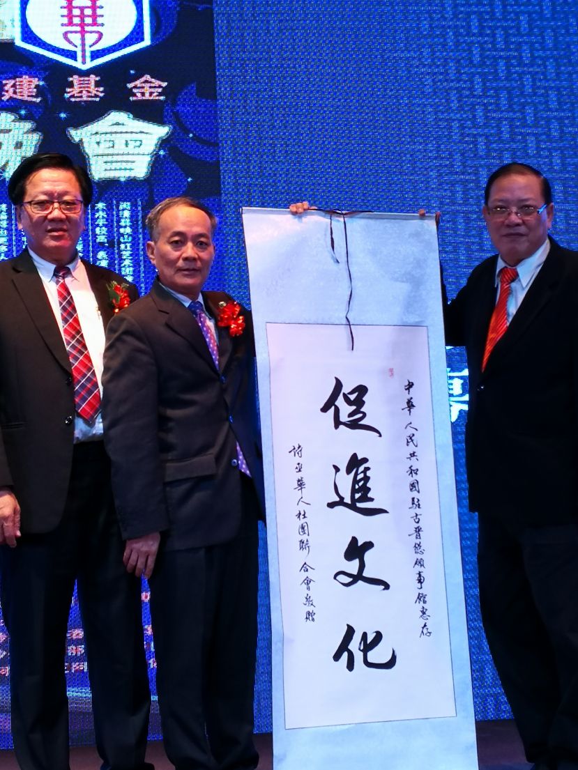 诗巫省华人社团联合会敬赠中国驻古晋总领事馆一面&ldquo;促进文化&rdquo;的条幅，由程洪领事（左二）代表接收。左一是华团会长严榀胜，右一是署理会长刘锦虎。