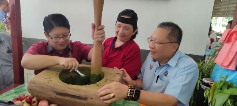 联邦企业及合作社部长拿督依温贝尼迪（左）体验以木臼剁木薯叶时摄。