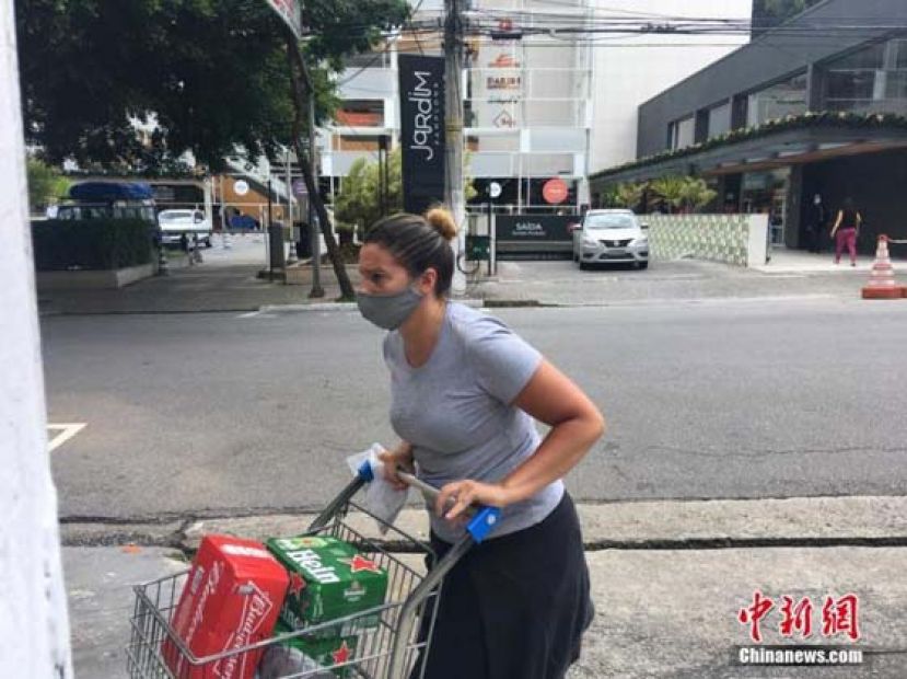 巴西圣保罗，一名妇女戴着口罩推着购物车过马路。