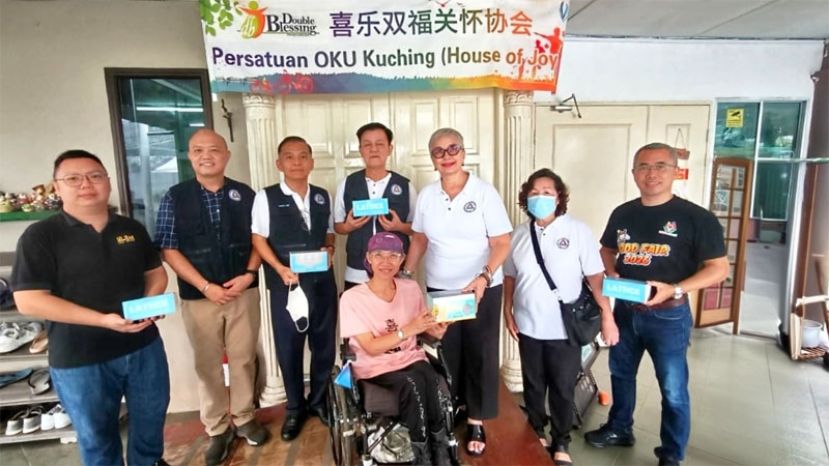 砂社会福利理事会会长拿汀斯里黄多娜（右三）与一众理事移交口罩给喜乐双福关怀协会创办人沈秋香老师（坐轮椅者）。