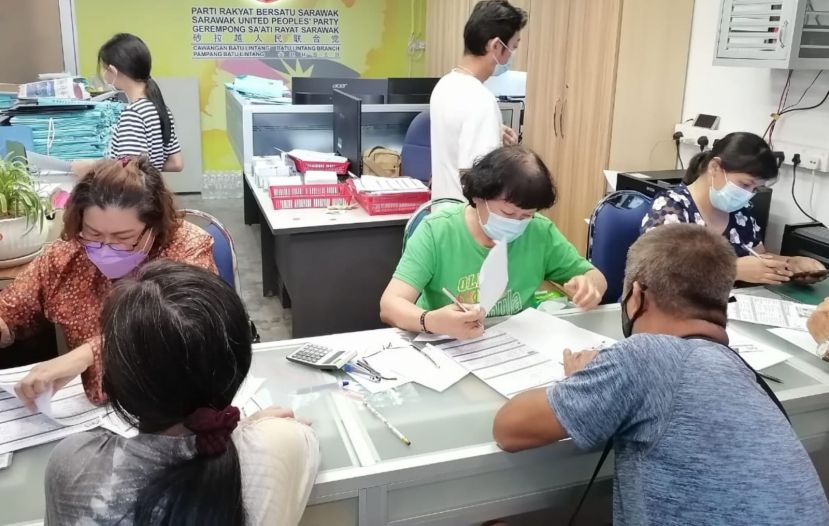 甲必丹何月明（左）与义工在人联党峇都林当支部为民众填写“爱心援助金”申请表格。