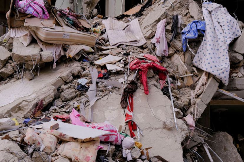 家用物品散落在混凝土废墟中，许多人仍被压在底下。