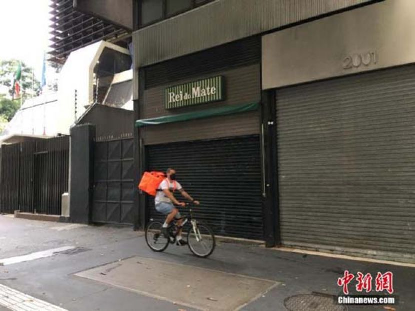当地时间5月1日,在巴西圣保罗,一名快递员骑车从几间关门的店铺前经过。受疫情影响,当地街上商店紧闭,行人稀少。