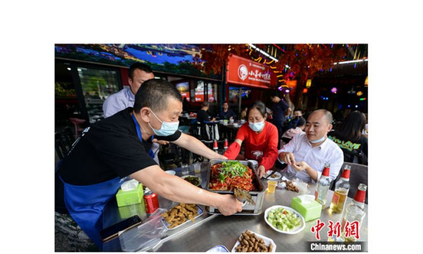 烤鱼店内工作人员为食客端上烤鱼。