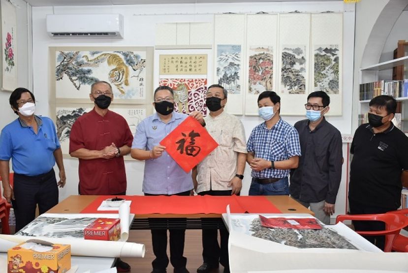 古晋南市市长拿督黄鸿圣（左三）为&rdquo;揮春庆虎年&rdquo;挥毫。左二为古晋中华文化艺术促进協会会长陈华敏、副会长许庆喜硕士（右四）及书法家们合照。