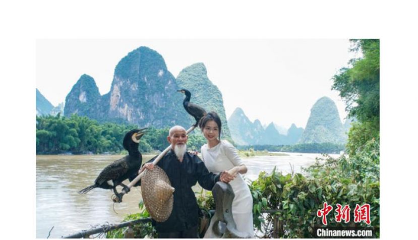 在桂林市阳朔县兴坪镇二十元人民币背景图案最佳摄影点，游客与黄月创合影。
