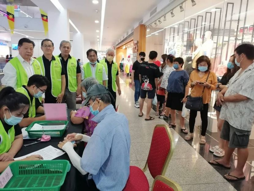 砂医总会长兼亚洲中医技职学院院长江宗兴（右）在美里义诊现场为各族看诊；后排右3为美里长生会会长张永源。